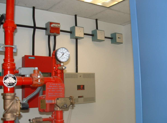 Red fire-suppression pipe system with gauges and control boxes on a wall in a utility room