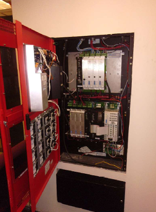 Open electrical panel with wiring and circuit boards inside a red cabinet
