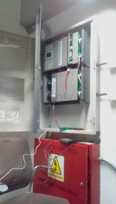 Open electrical control cabinet with wiring and a red warning box inside a utility room