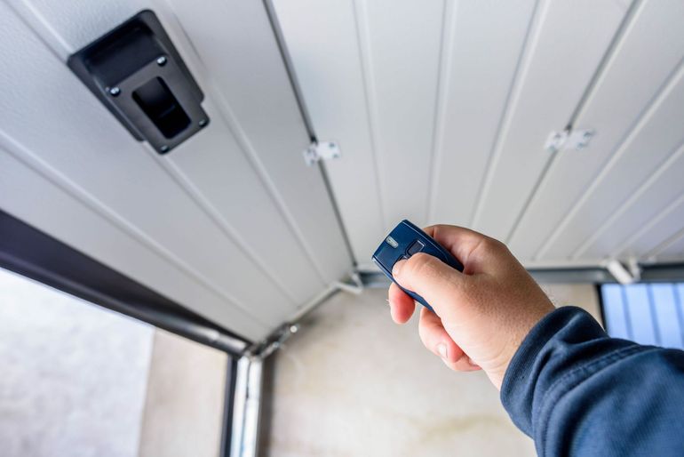 Hand holding garage door opener, pointing towards the ceiling-mounted receiver as the door opens.