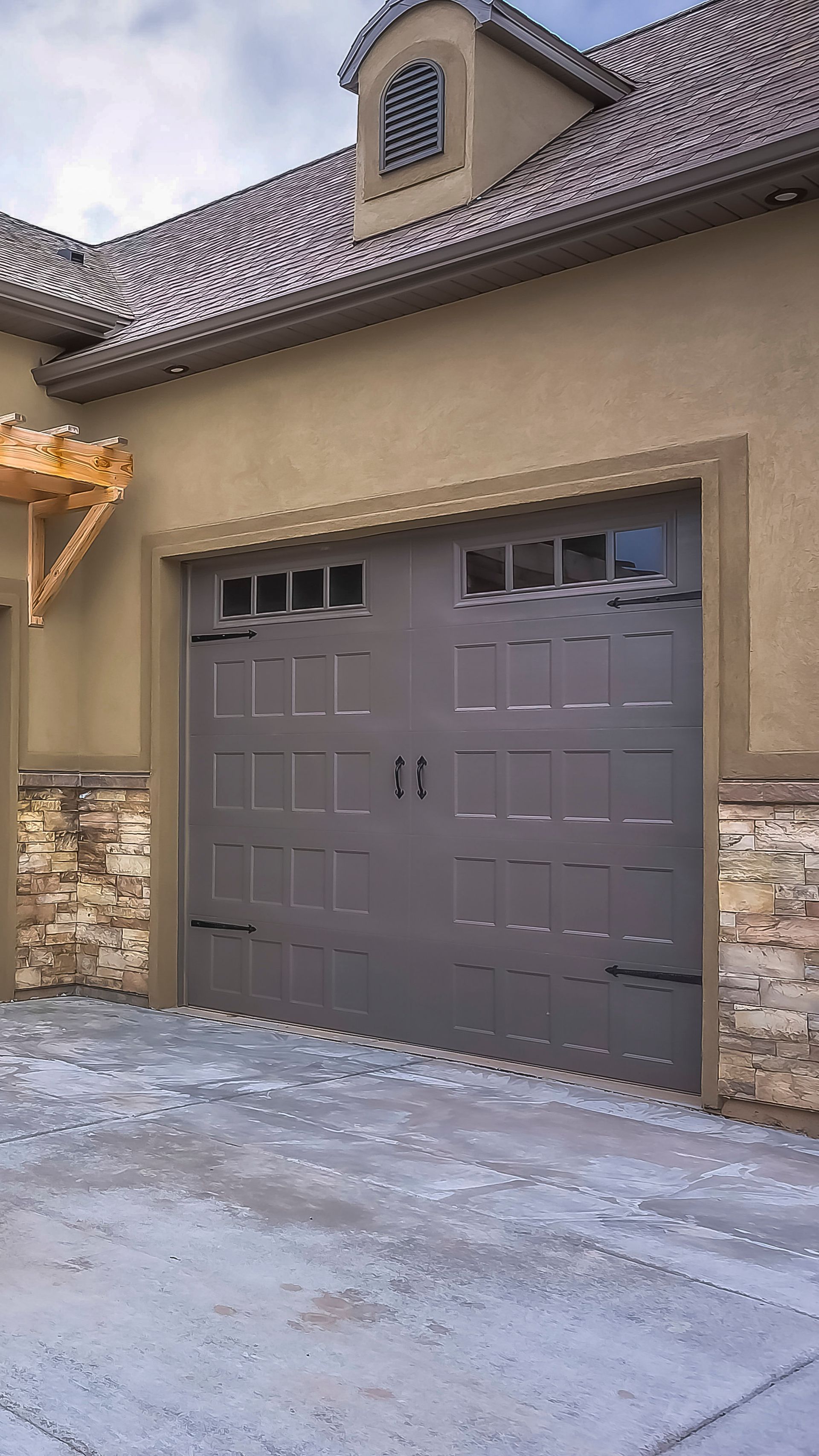 Tan house exterior with a gray double garage door and stone accents, viewed from the driveway