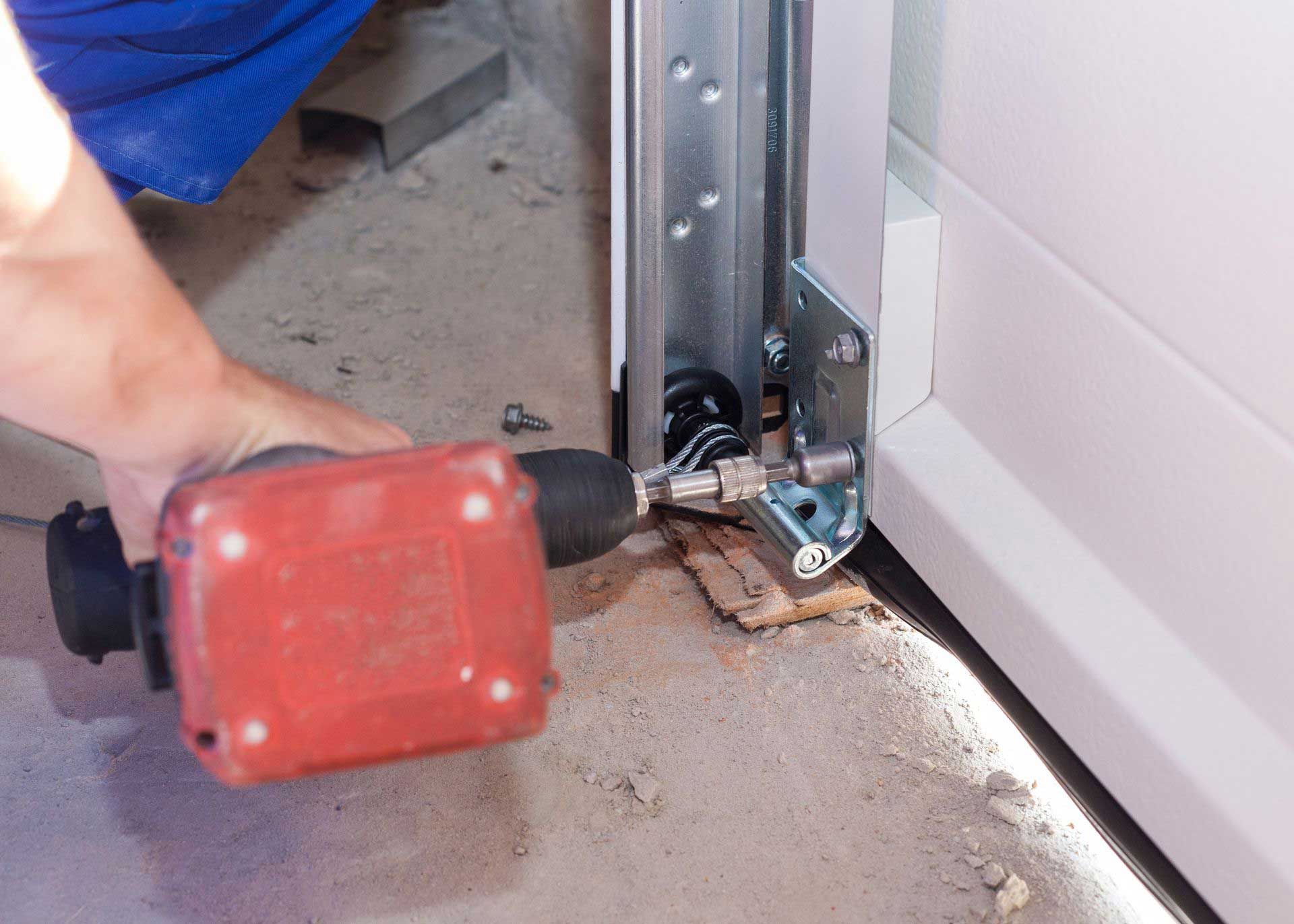 Person using a red drill to install a garage door component on a concrete floor.