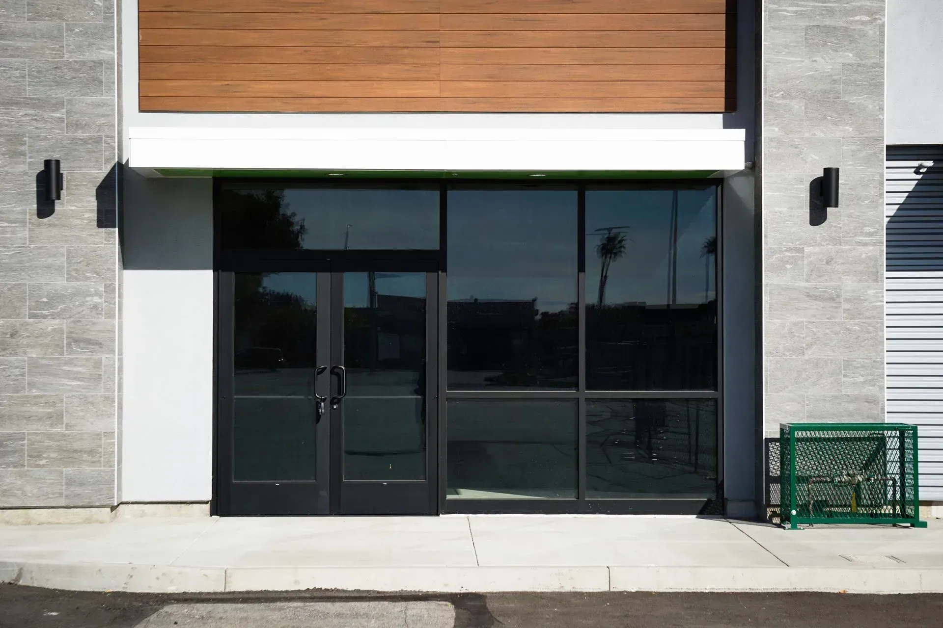 Exterior storefront with black-framed windows and doors, tan wood paneling, and gray stone siding.