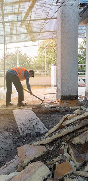A construction worker is raking the ground with a shovel.