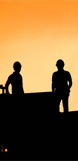 Two construction workers are standing on top of a building at sunset.