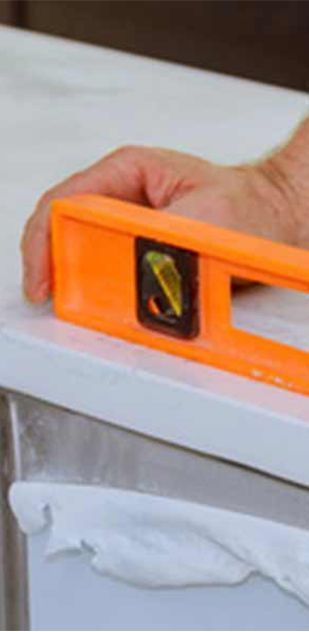 A person is measuring a piece of wood with an orange level.