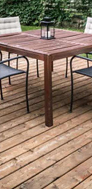 A wooden table and chairs are on a wooden deck.