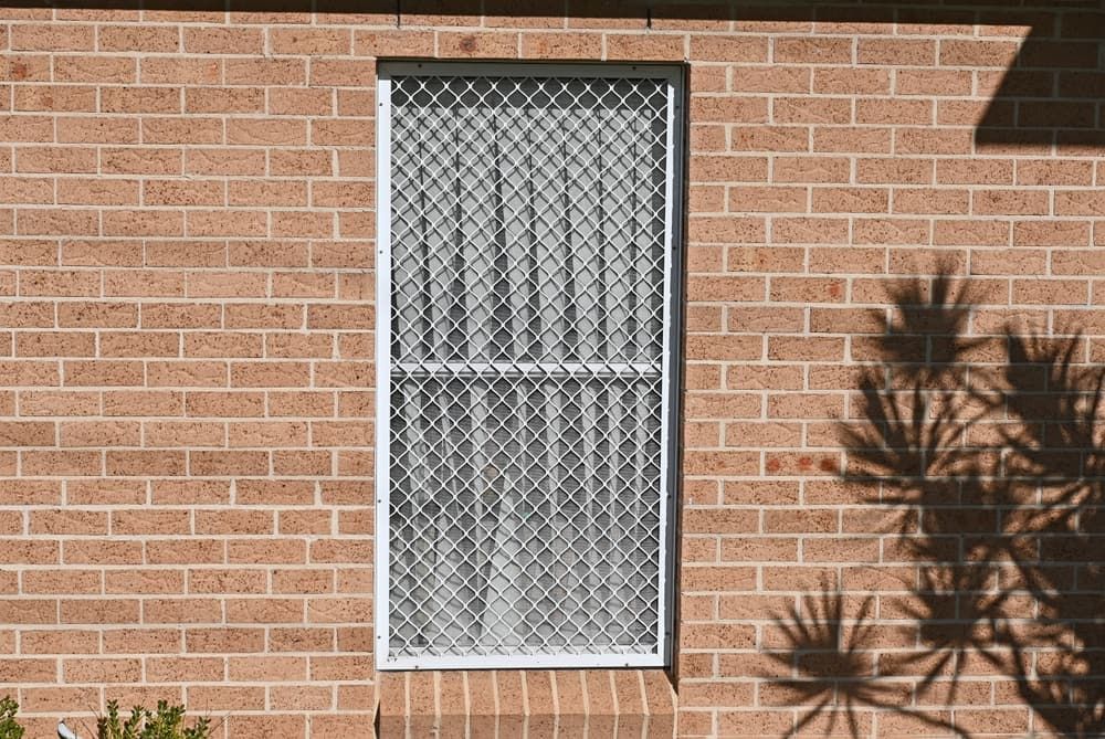 A Brick Wall With a Window With a Chain Link Fence Around It — Whitsunday Screens & Grilles In Airlie Beach, QLD