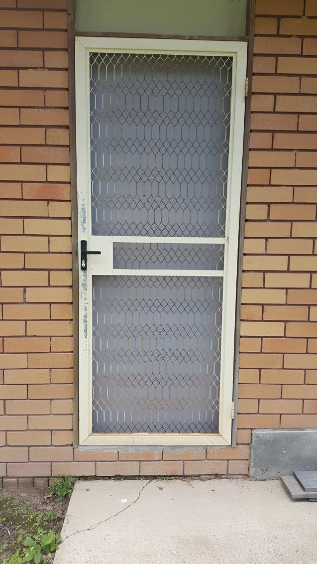 A White Screen Door is Sitting on a Brick Wall — Whitsunday Screens & Grilles In Proserpine, QLD