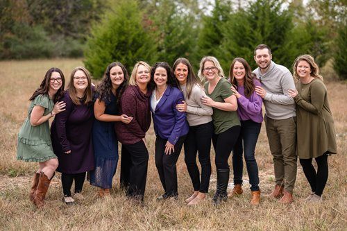 Pediatric staff at Nurture Pediatrics. They are standing together in a park with trees in the background.