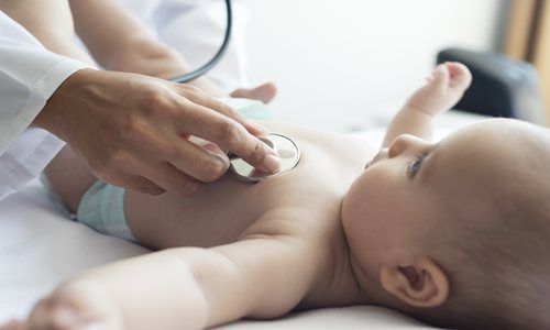 A healthcare provider uses a stethoscope to examine a baby's chest while the infant lies on an examination table.