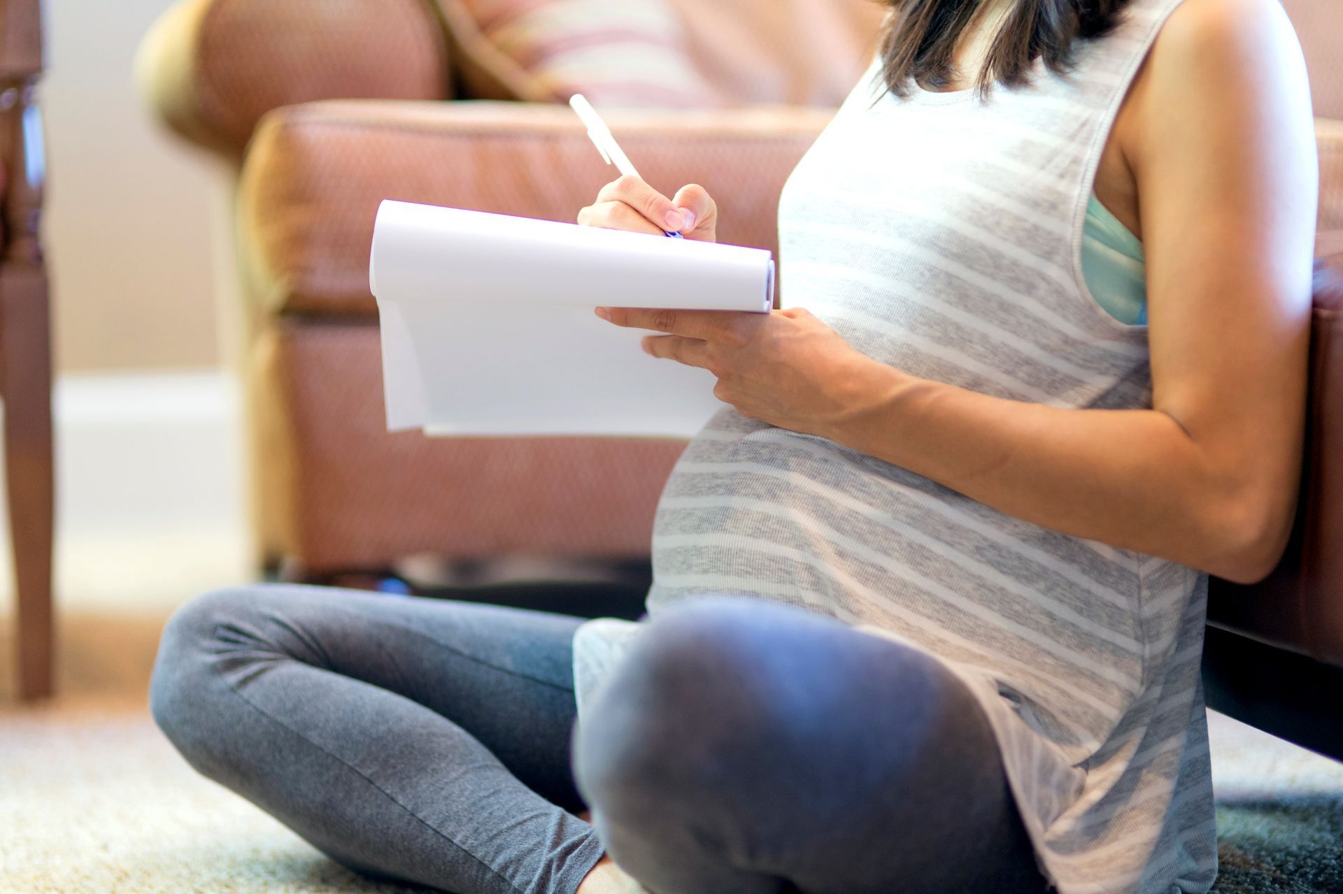 Person sitting on the floor, writing in a notebook near a sofa.