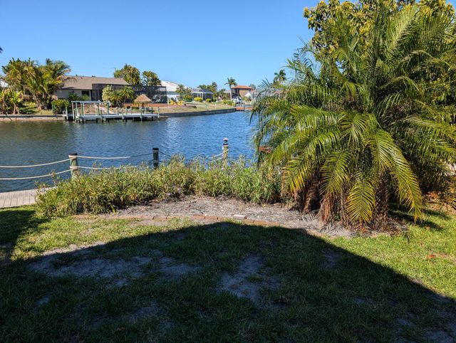 Sunny waterfront yard with palm trees, grass, and a canal view across the water