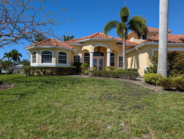 Single-story cream house with red tile roof and arched porch, viewed from a grassy front yard under a clear blue sky