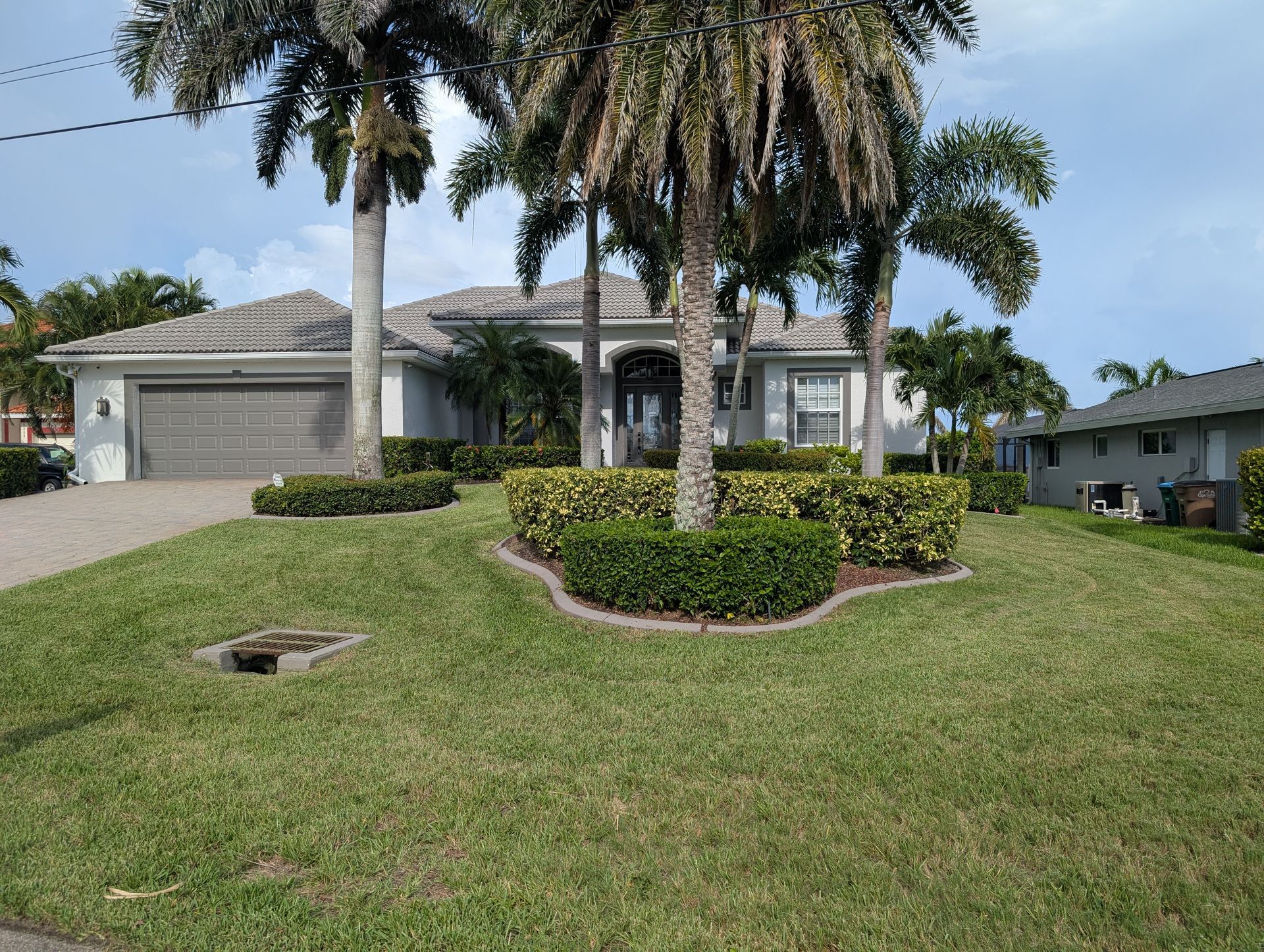 Single-story suburban house with a manicured lawn and tall palm trees under a clear sky