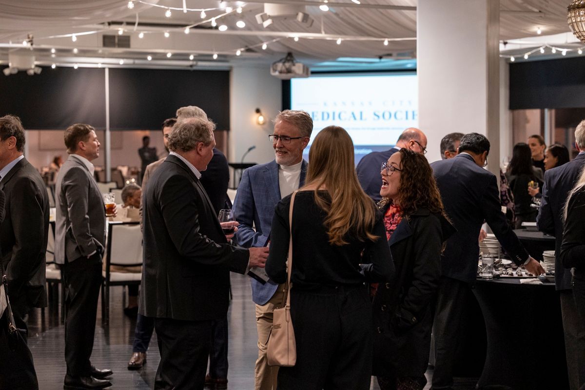 People in business attire at an event, socializing and networking. A screen displays 
