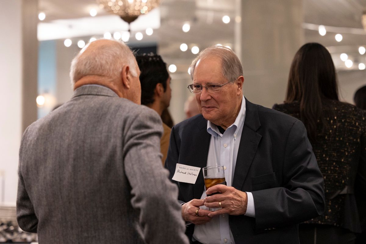 Two men in suits conversing at an event, one holding a drink.