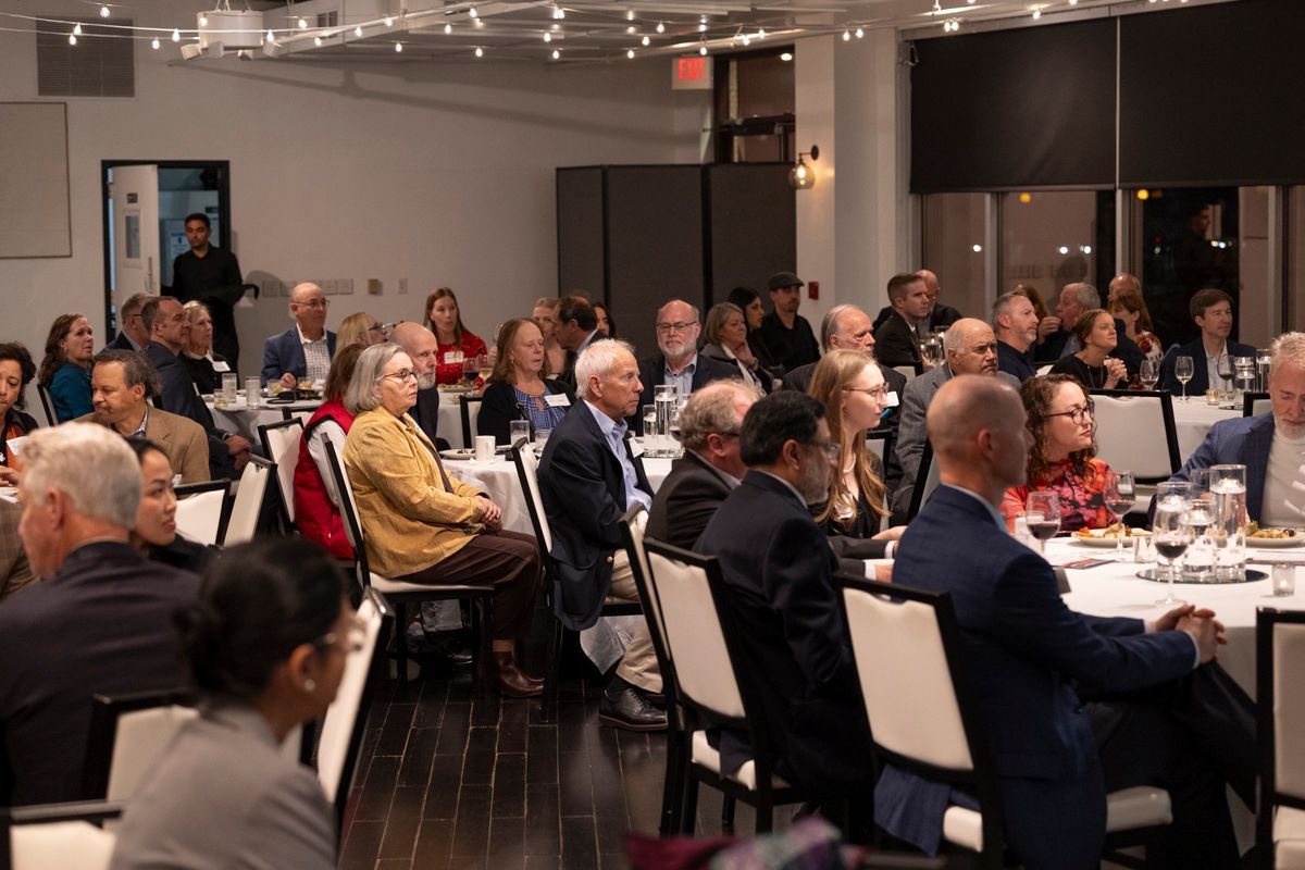 People seated at round tables in a brightly lit room, attending an event.