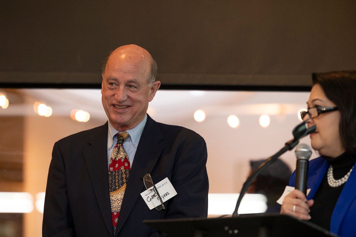 Man in suit smiles near a woman holding a microphone; both stand at a podium indoors.