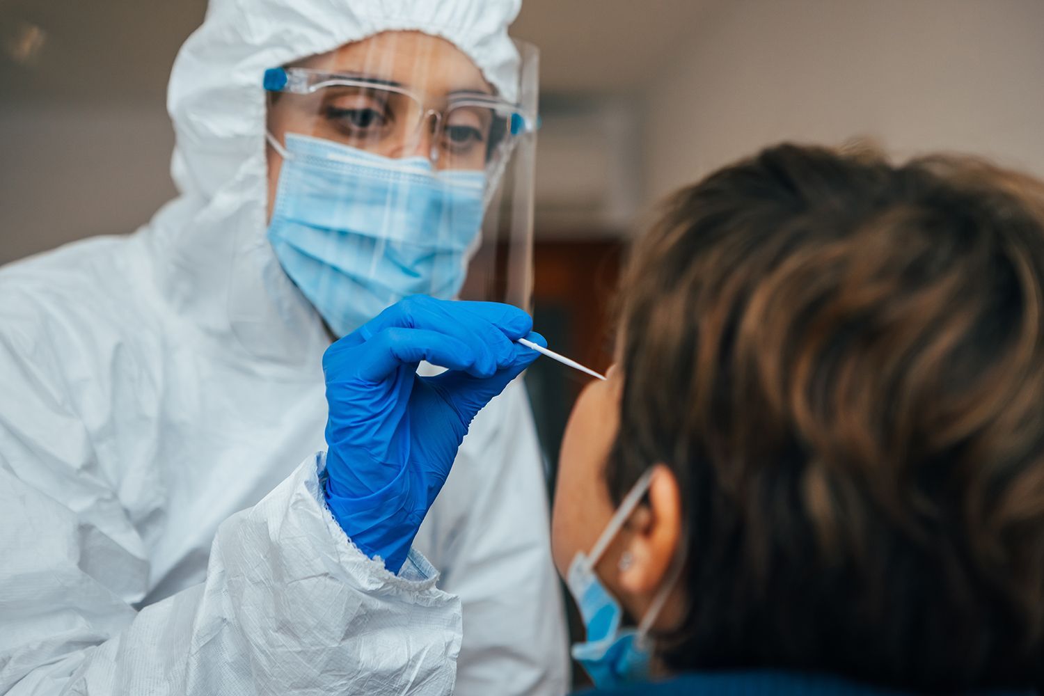 A woman in a protective suit is taking a sample from a patient 's nose.
