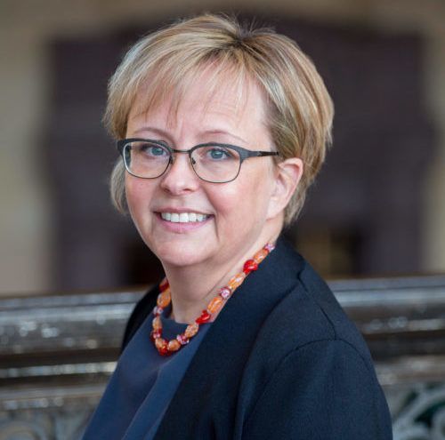 A woman wearing glasses and a necklace is smiling for the camera.