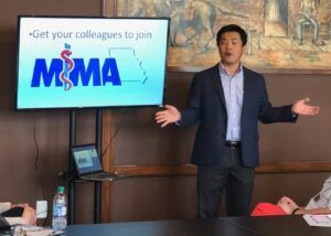 A man is giving a presentation in front of a screen that says mma.