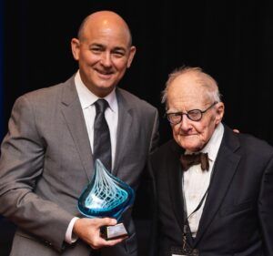 Two men in suits are standing next to each other holding a trophy.