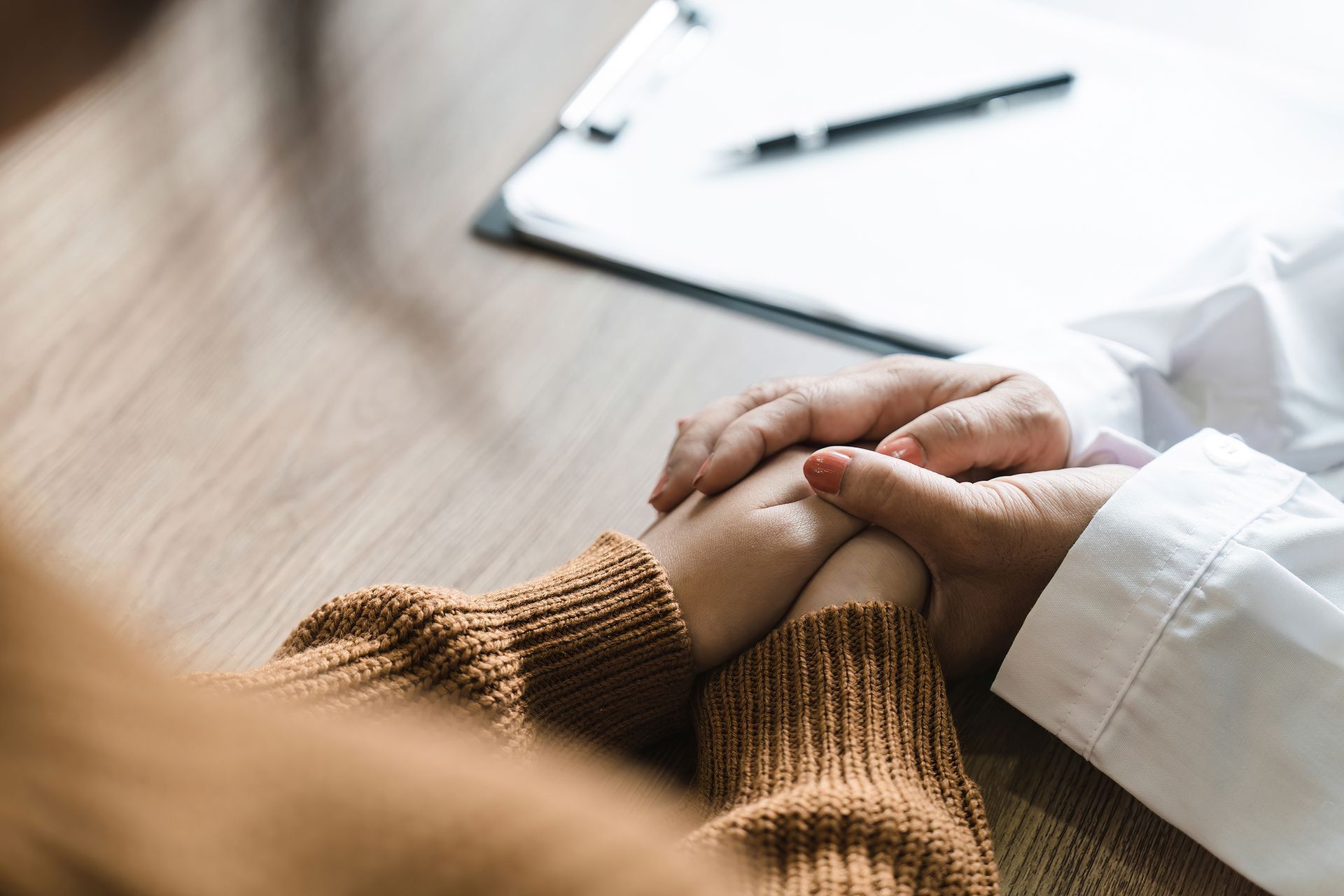 A doctor is holding a patient 's hand while sitting at a table.