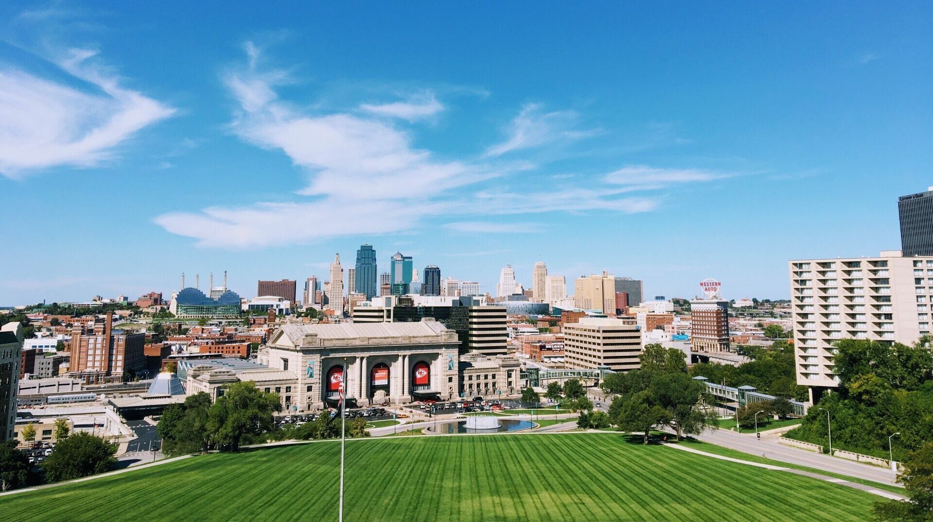 An aerial view of a city skyline with a lush green field in the foreground.