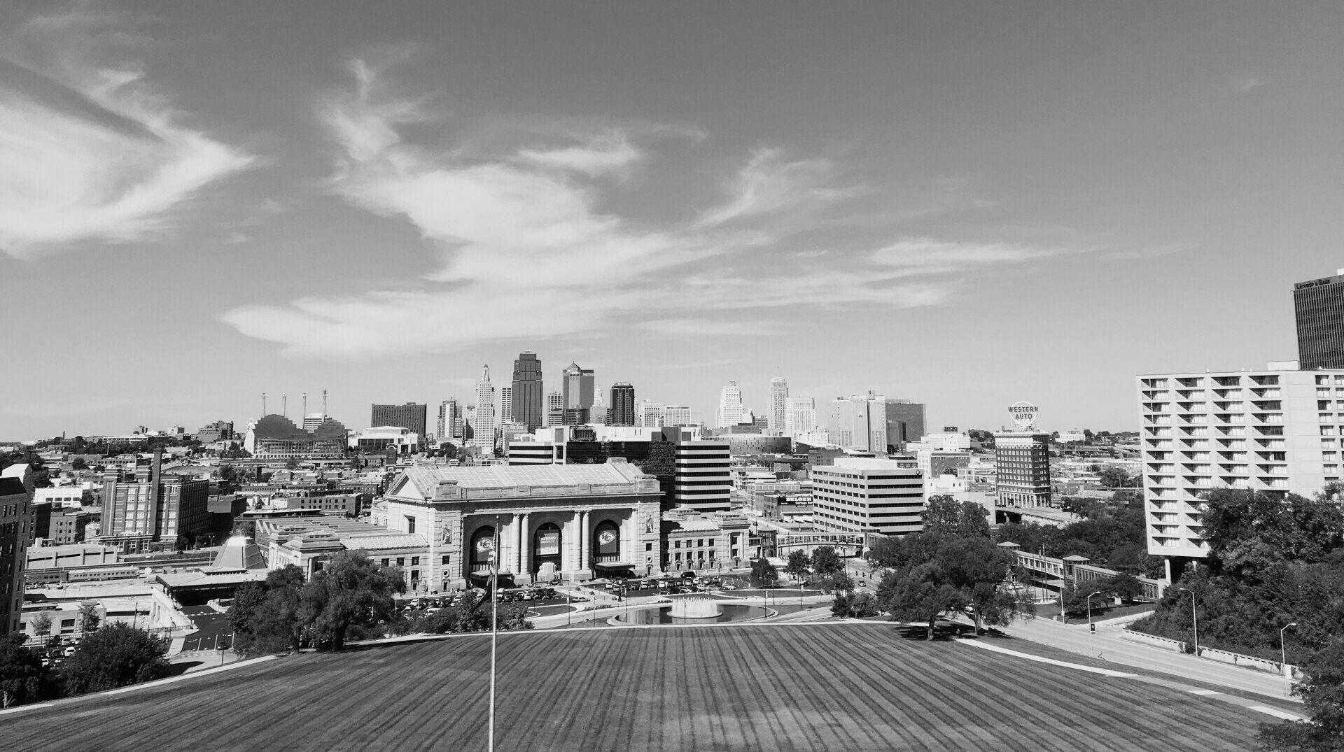 Skyline view of Kansas City, Missouri, including Union Station, with a field in the foreground under a cloudy sky.
