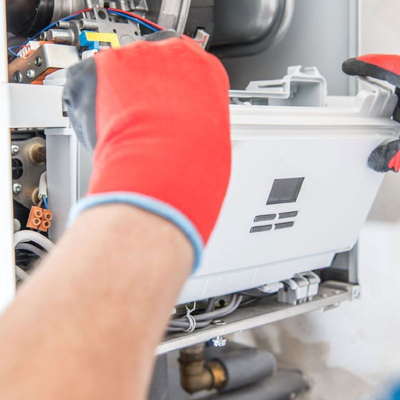 Person in red gloves working on a white appliance, likely a furnace, in a home.