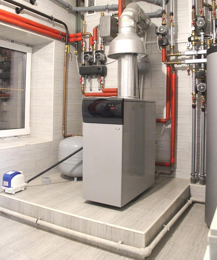 Heating system in a utility room with pipes, boiler, and air pump.