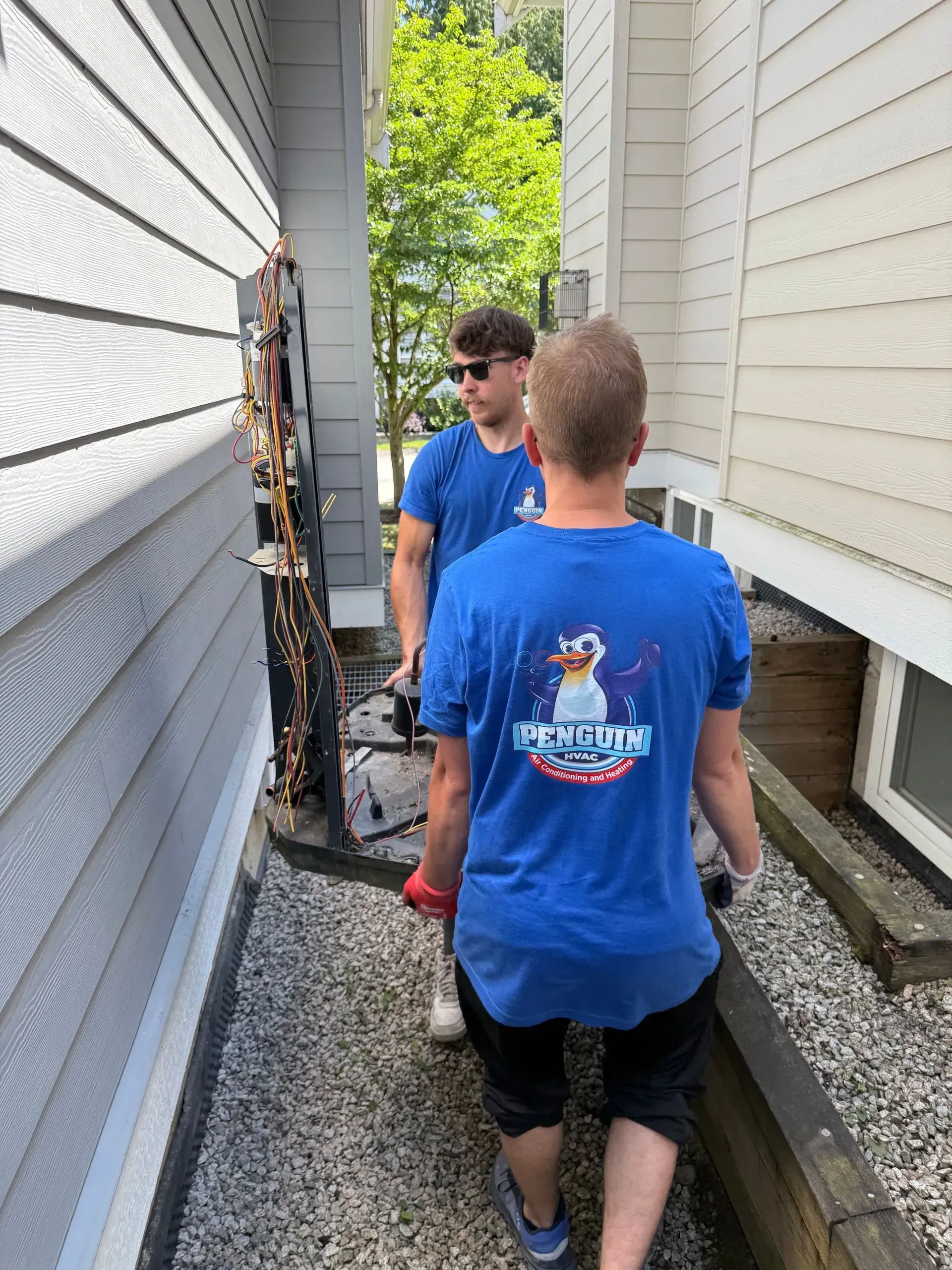 Two people in blue matching shirts work in a narrow gravel path between two house walls.