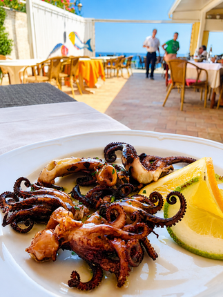 Polpo grigliato al limone servito su un piatto sulla terrazza di un ristorante sul mare.
