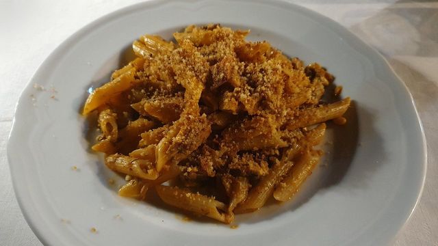 Piatto di pasta al sugo di pomodoro e formaggio grattugiato su un piatto bianco.