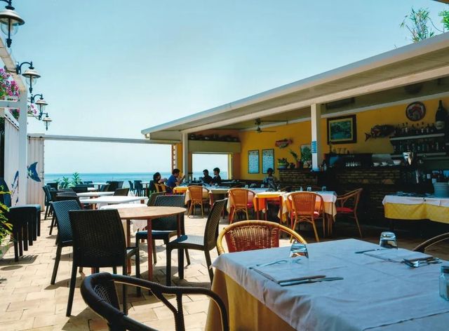 Terrazza del caffè sul lungomare con tavoli, sedie e vista sull'oceano sotto un cielo soleggiato.