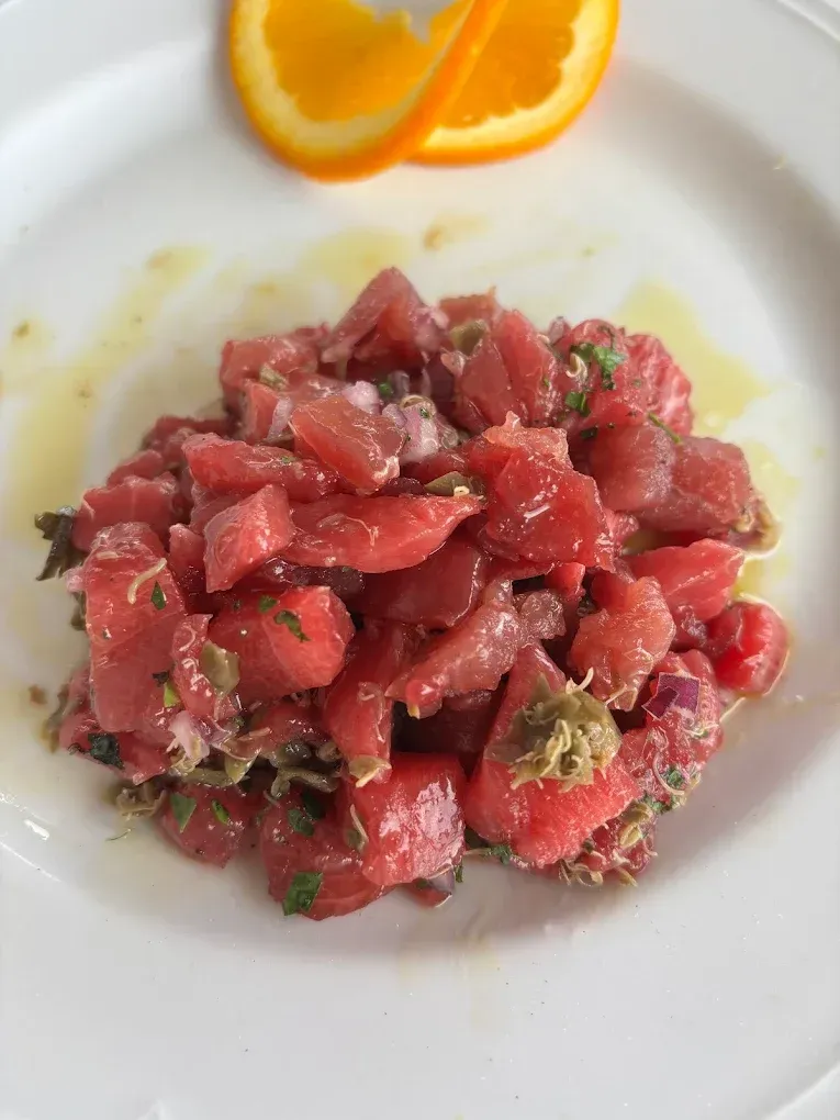 Tartare di tonno a cubetti con erbe aromatiche su un piatto bianco, guarnita con fette d'arancia.