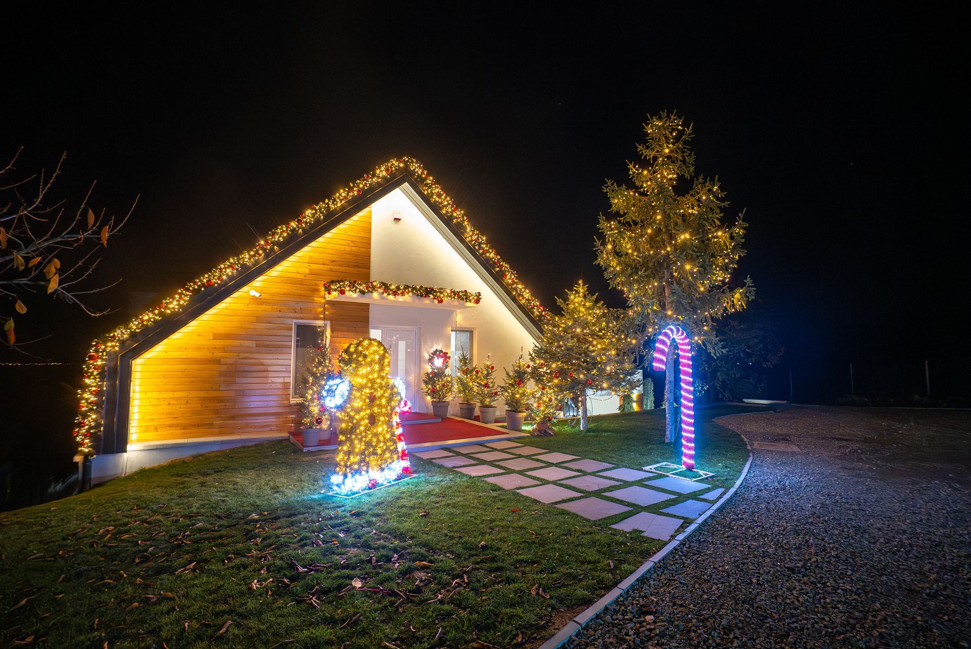 Holiday-lit house at night with glowing trees, a lit walkway, and festive decorations
