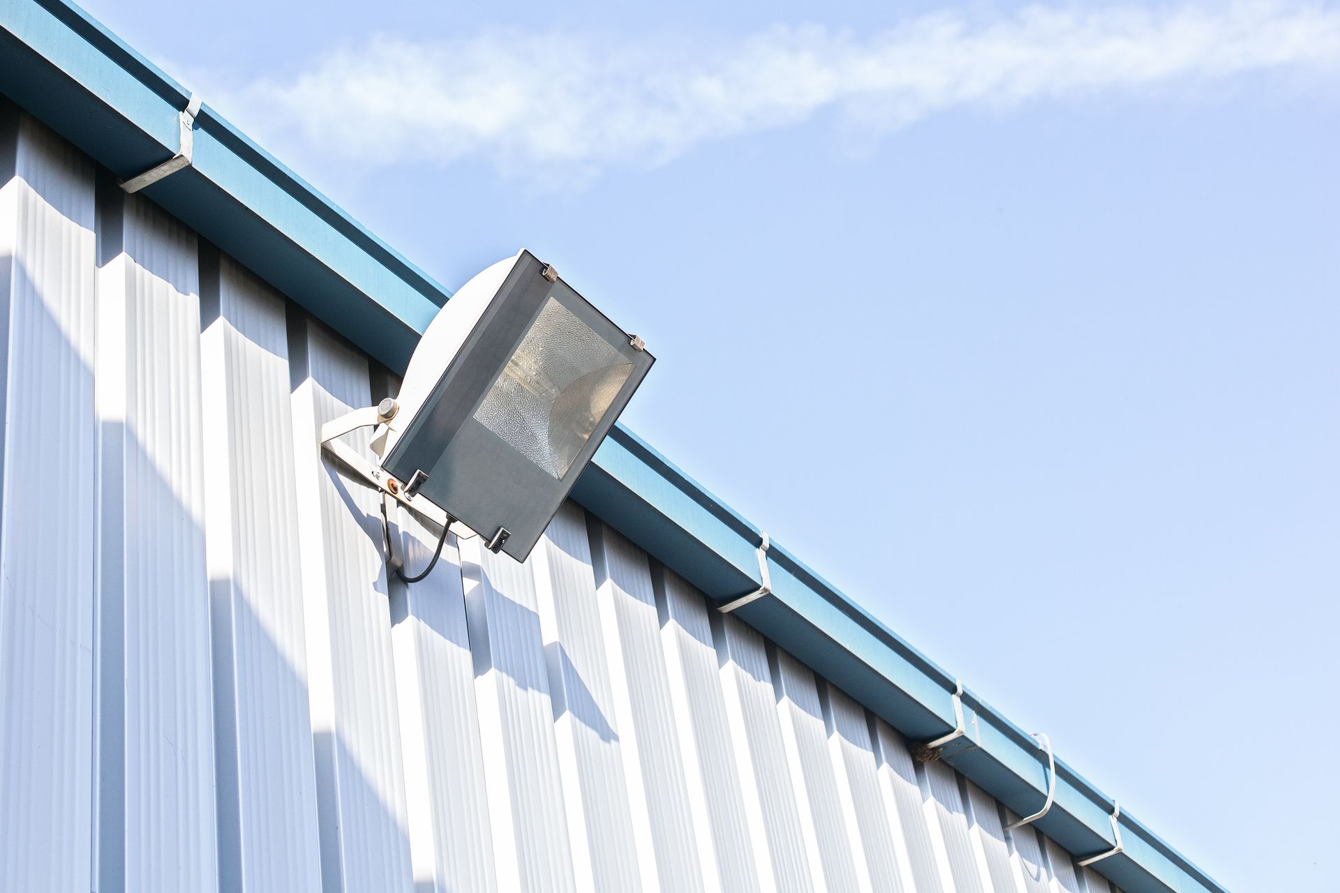 Wall-mounted floodlight on a white metal building against a blue sky