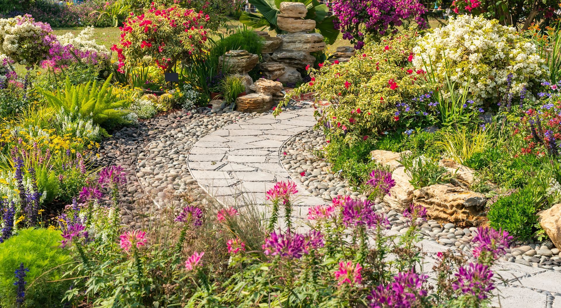 Stone garden path winding through lush flowering plants in pink, yellow, and white.