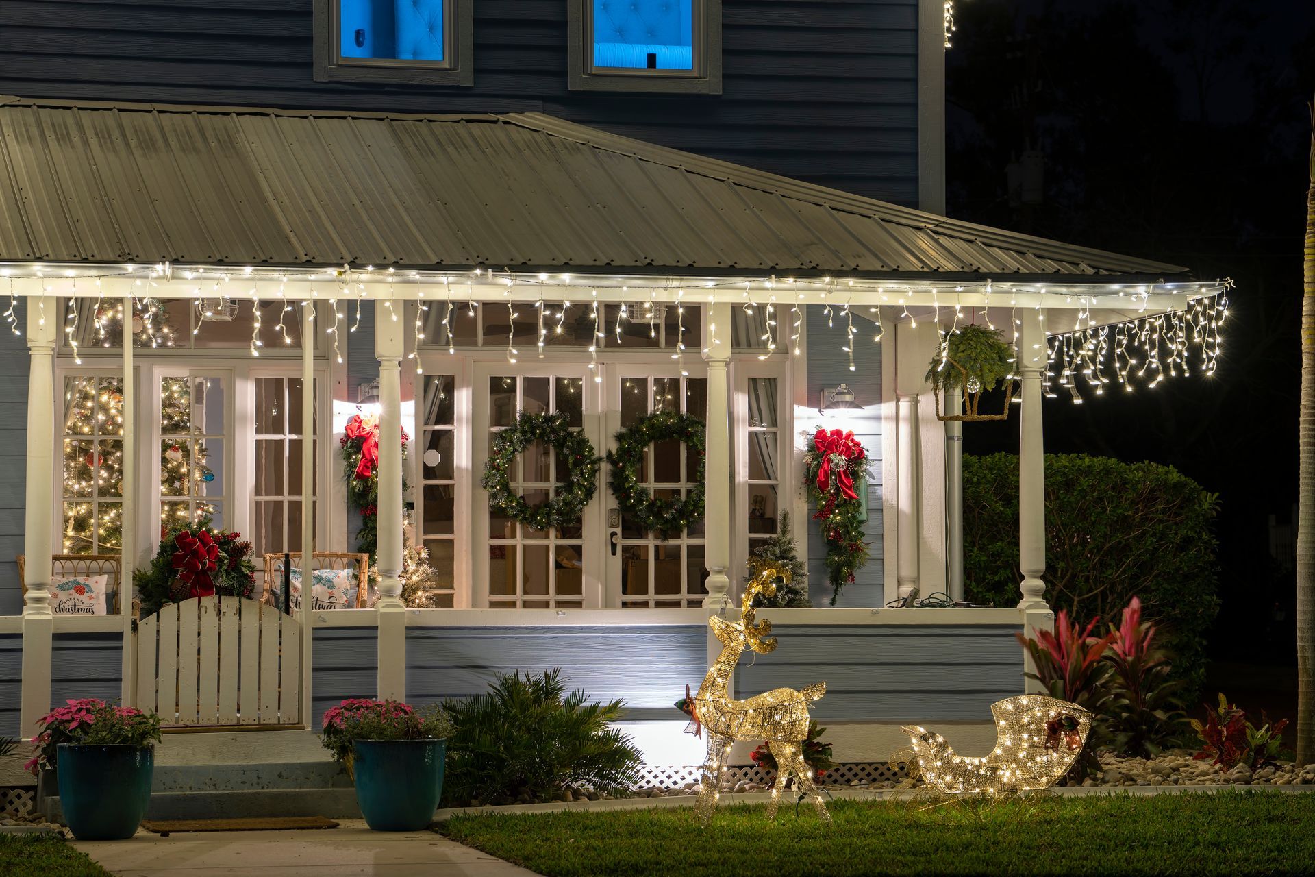 House porch decorated with white Christmas lights, wreaths, and glowing reindeer at night
