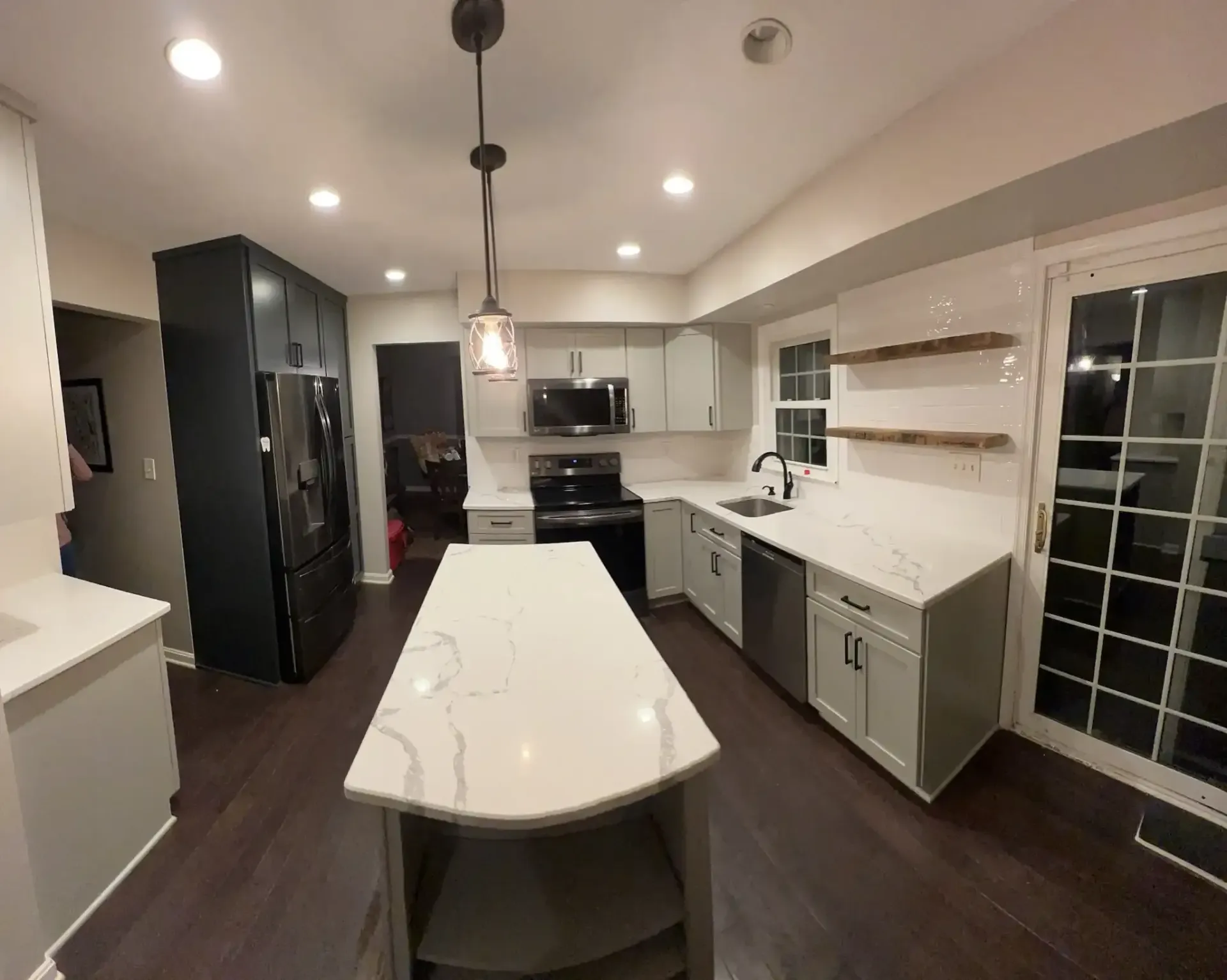 Modern kitchen with white island, dark cabinets, pendant lights, and a large windowed dining area