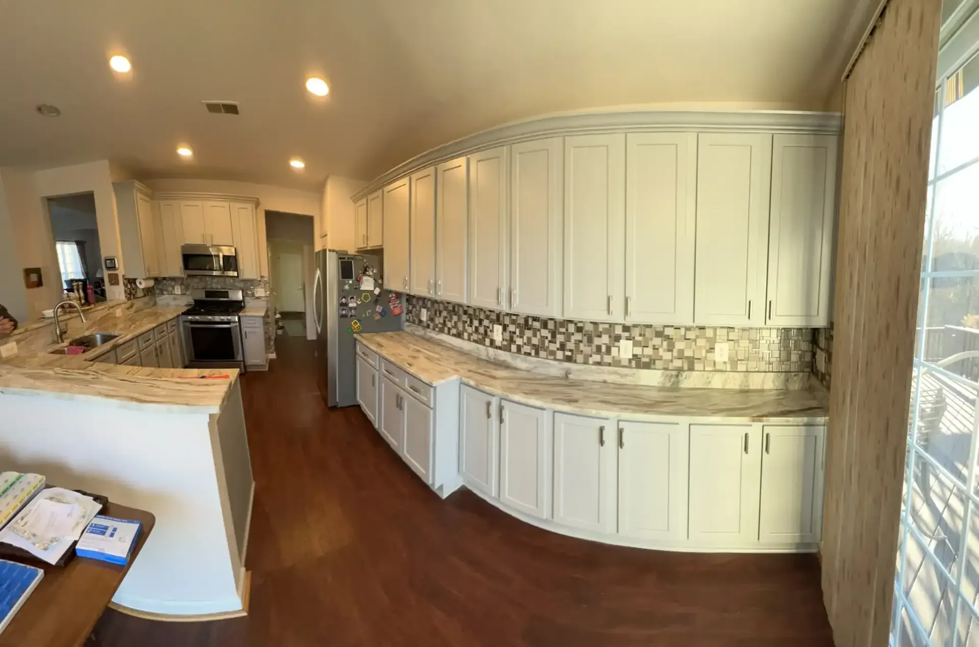 Wide kitchen with white cabinets, granite countertops, wood floors, and a large island under recessed lighting.