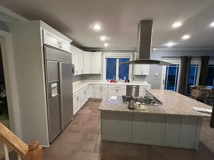 Modern kitchen with white cabinets, granite island, stainless fridge, and tile floor