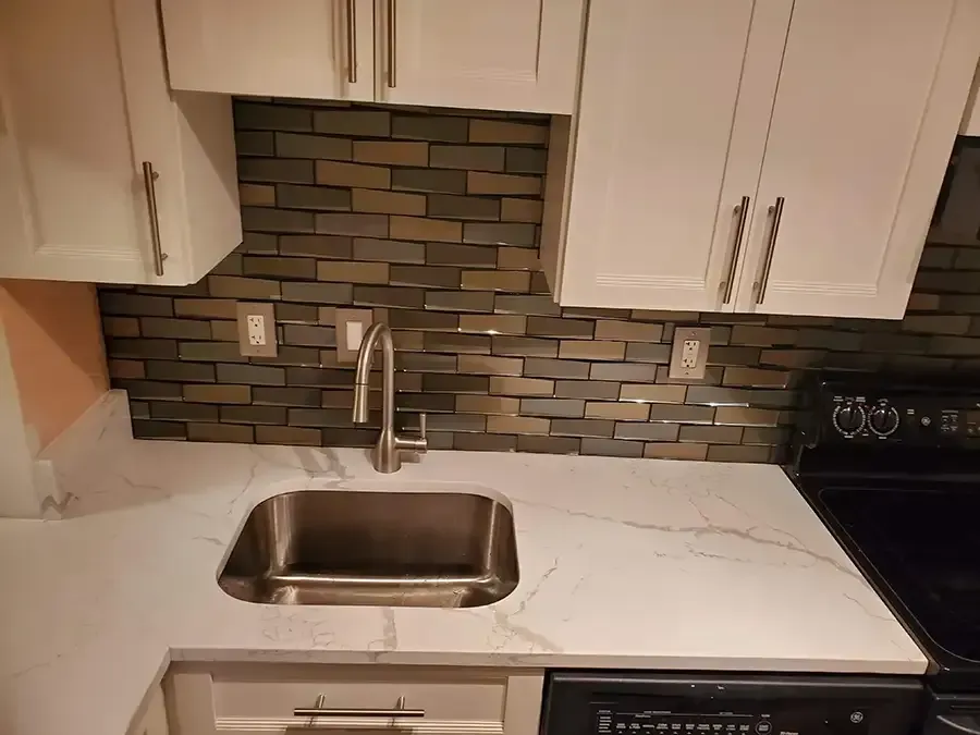 Kitchen sink with white counters, mosaic tile backsplash, and white cabinets above a black stove.