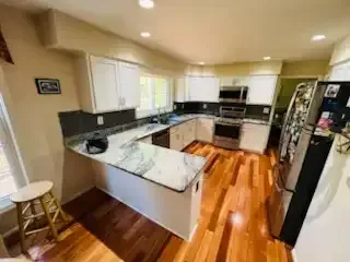 Bright kitchen with white cabinets, black appliances, marble counters, and hardwood floors