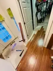 Hallway with broken wooden floorboards, a vacuum, and scattered tools near a bathroom and closet.