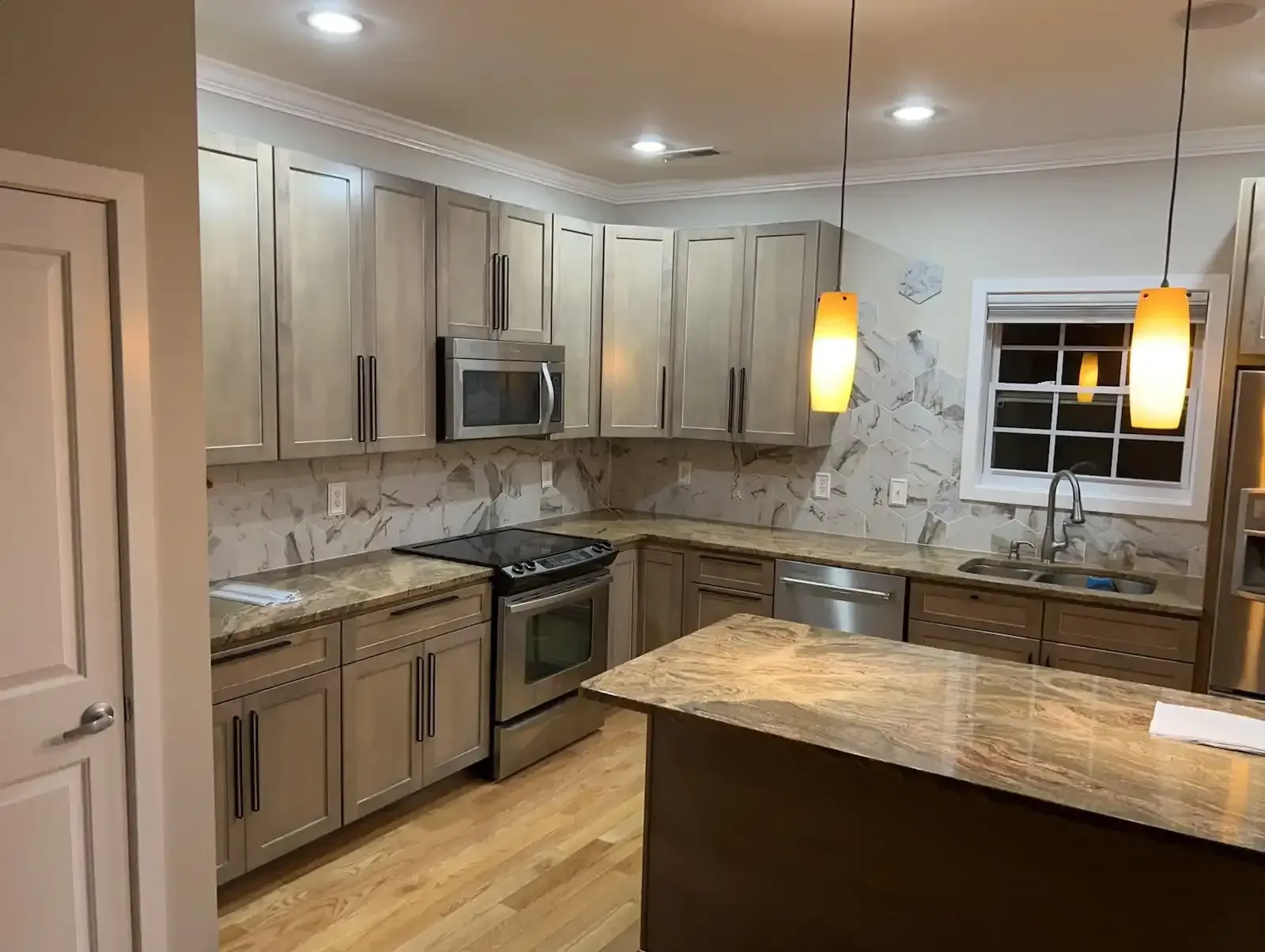 Modern kitchen with light wood cabinets, granite countertops, stainless appliances, and pendant lights over an island.