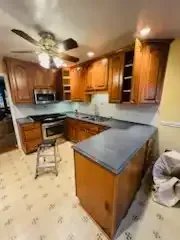Small kitchen with wood cabinets, gray countertops, tiled floor, ceiling fan, and a step stool near the sink.