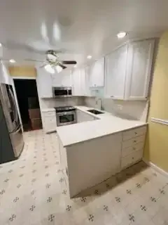 Bright white kitchen with island, stainless appliances, ceiling fan, and patterned tile floor